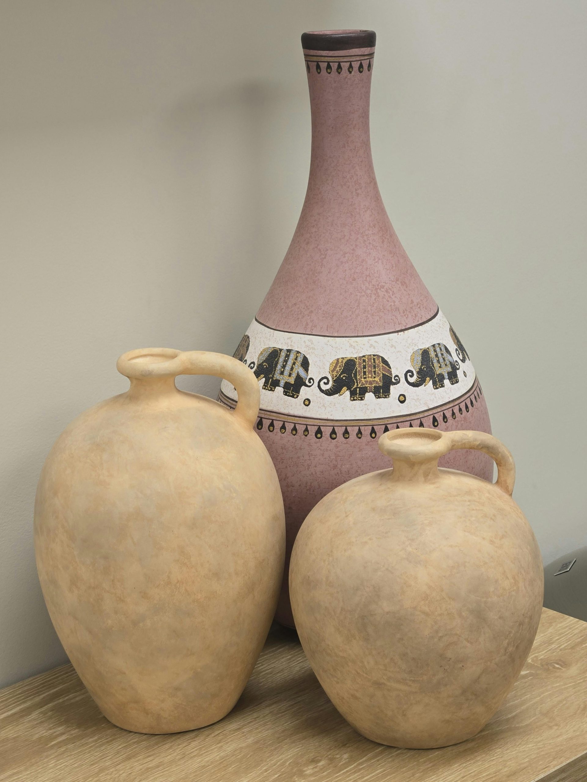 Three decorative ceramic jugs on a wooden surface featuring elephant motifs.